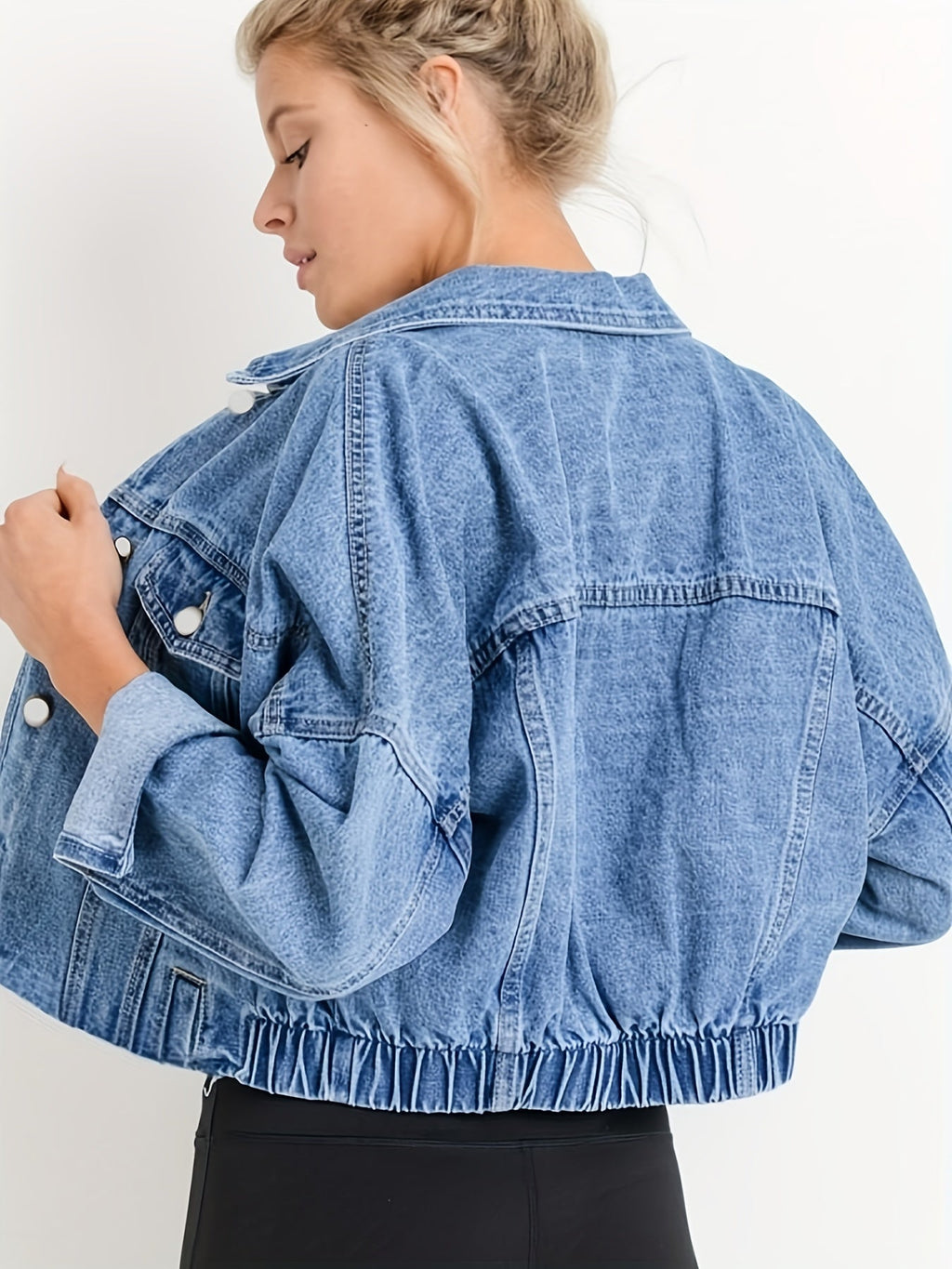 Femme portant une veste en jean bleu oversize, manches retroussées, sur fond blanc. Mode décontractée, tendance denim, style moderne.