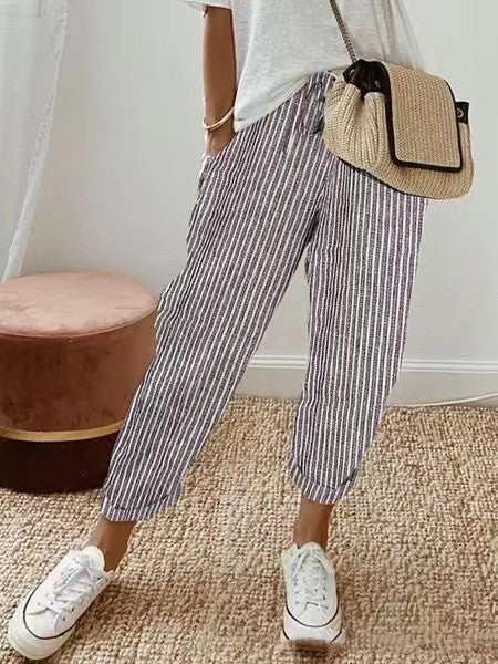 Femme portant un pantalon rayé blanc et noir, t-shirt blanc, baskets blanches, sac en osier. Mode décontractée, style estival, tenue confortable.