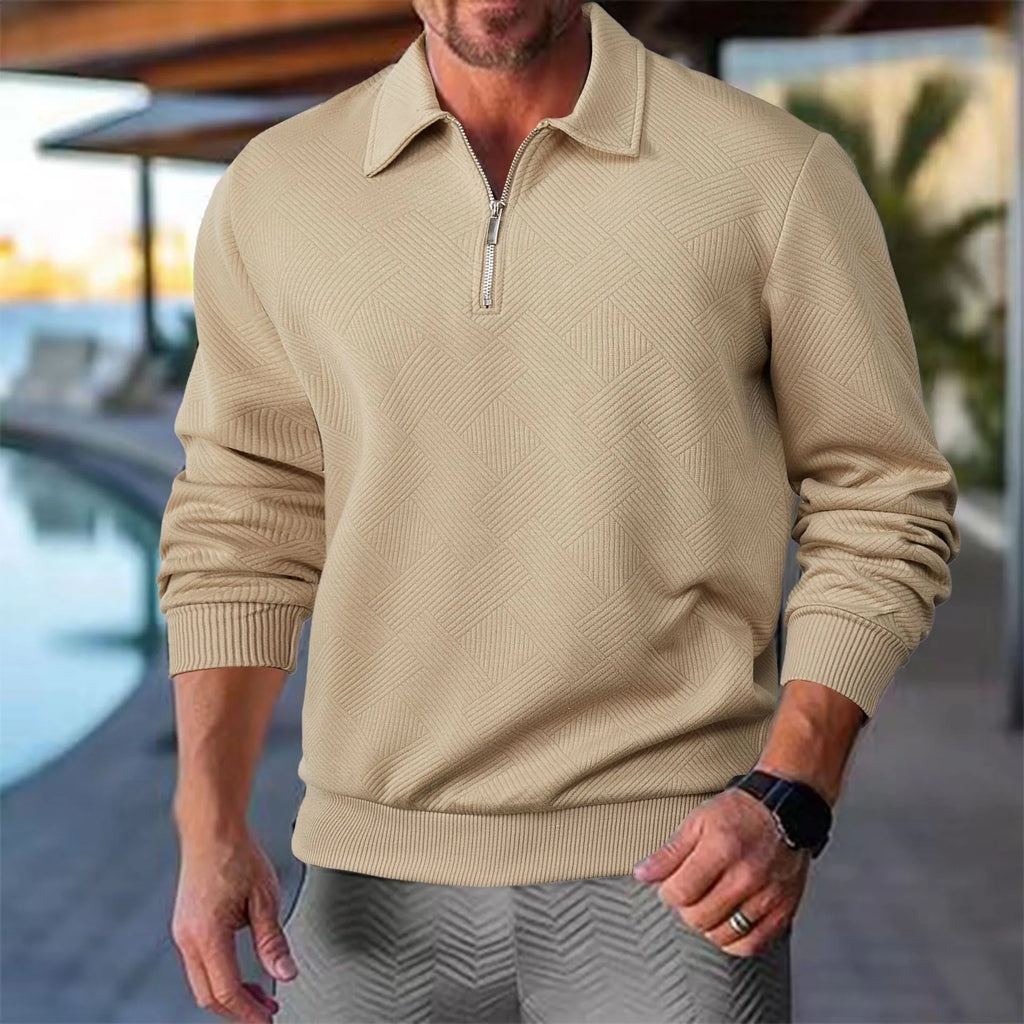 Homme portant un pull beige à col zippé, motif géométrique, près d'une piscine. Mode masculine élégante, tenue décontractée chic.