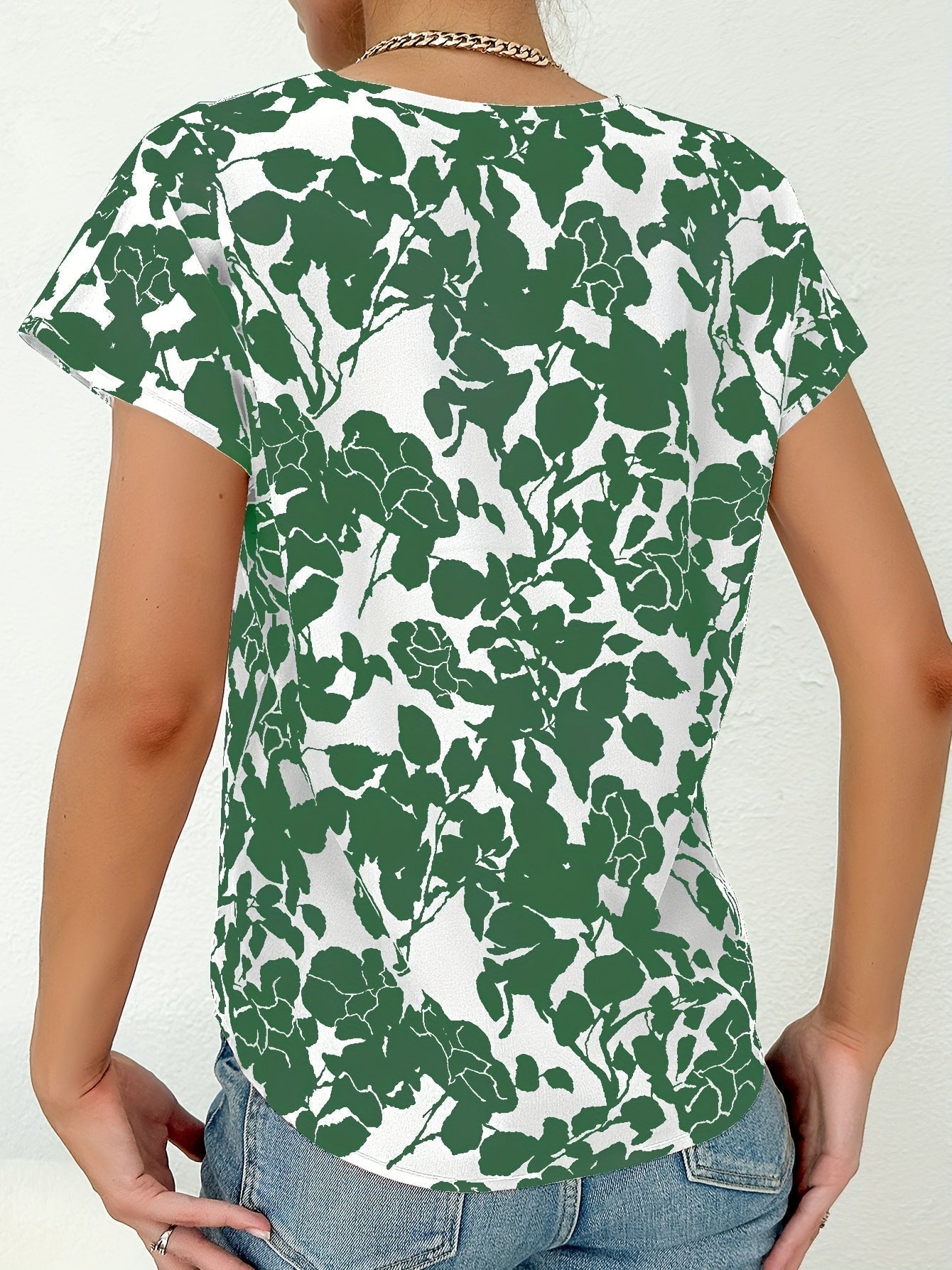 Femme portant un t-shirt à motifs floraux verts sur fond blanc, vue de dos. Mode décontractée, style estival, tendance vêtements imprimés.