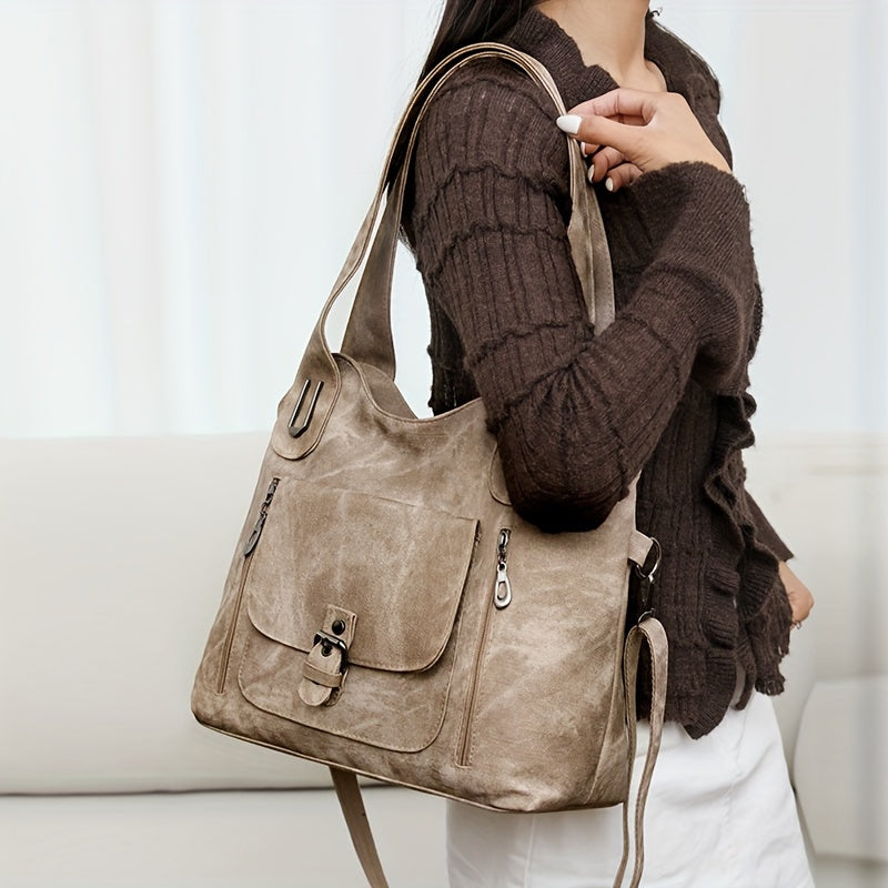 Sac à main en cuir beige porté par une femme en pull marron. Design élégant avec poche avant et fermeture à boucle. Accessoire mode tendance.