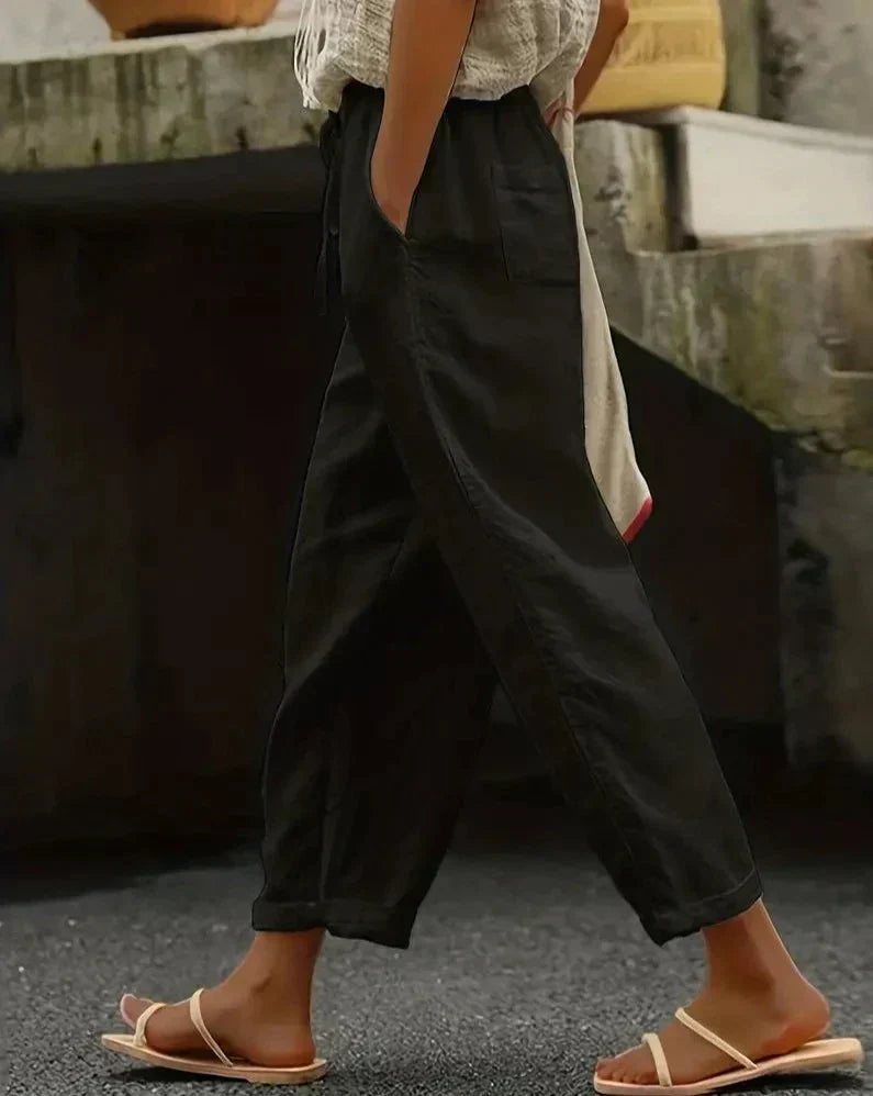 Personne portant un pantalon noir ample et des sandales beiges, marchant sur un trottoir. Mode décontractée, style estival, confort urbain.