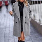 Femme portant un manteau gris en laine, col large, sur un pull noir, jupe en cuir, marchant en ville. Mode automne-hiver, élégance urbaine.