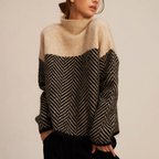 Femme portant un pull en laine à motif chevron noir et beige, col montant, manches longues. Mode automne-hiver, style décontracté et élégant.