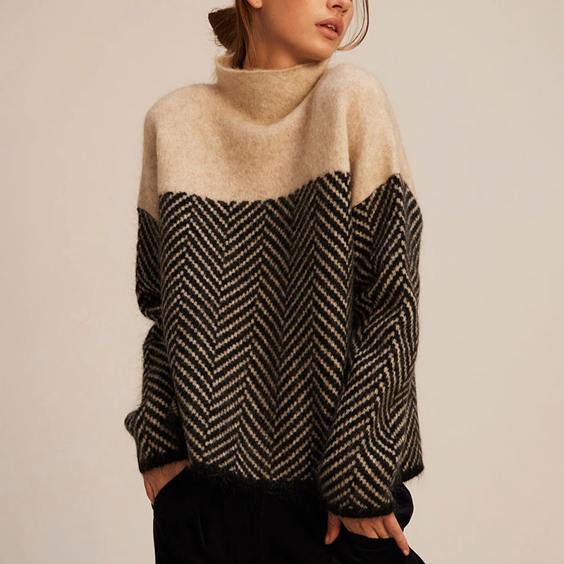 Femme portant un pull en laine à motif chevron noir et beige, col montant, manches longues. Mode automne-hiver, style décontracté et élégant.