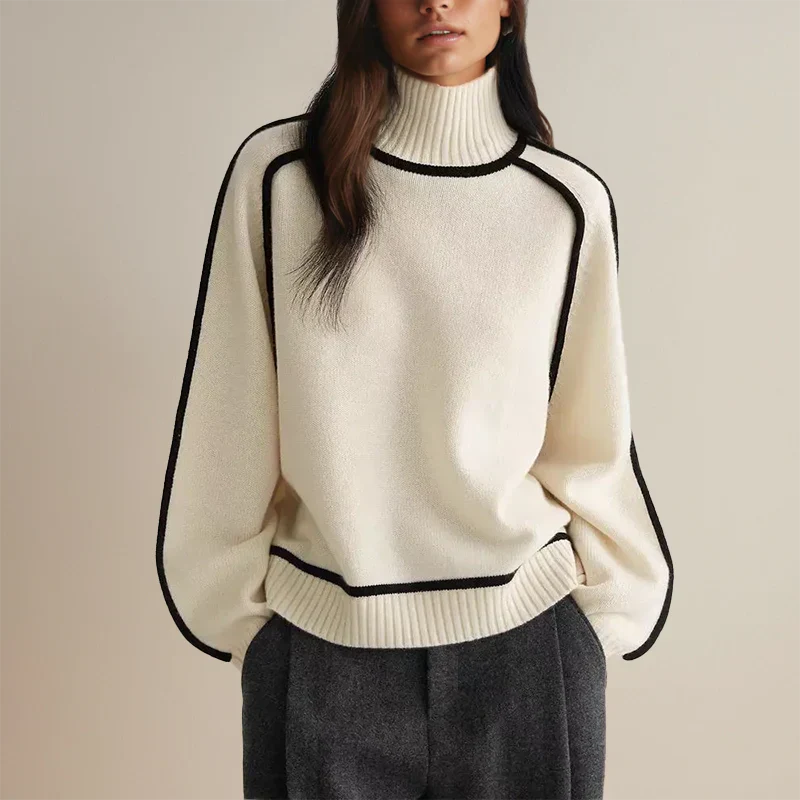 Femme portant un pull blanc à col roulé avec bordures noires, manches longues, associé à un pantalon gris. Mode automne-hiver élégante et moderne.