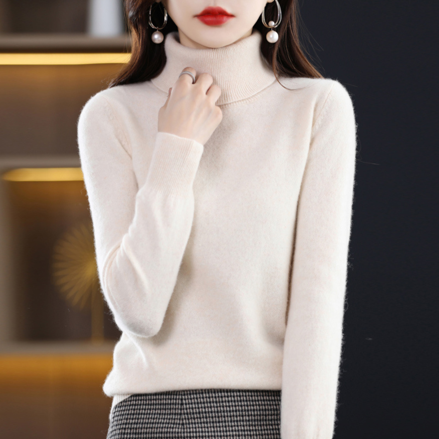 Femme portant un pull col roulé blanc en cachemire, élégante, avec boucles d'oreilles perles, mode automne-hiver, style chic et moderne.
