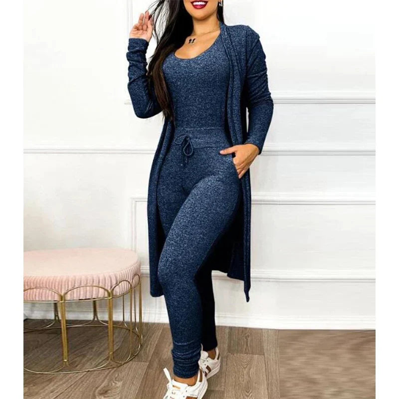 Femme portant une combinaison bleu foncé avec un long cardigan assorti, posant dans un intérieur moderne. Mode féminine, tenue décontractée élégante.