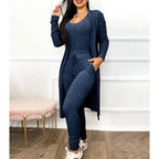 Femme portant une combinaison bleu foncé avec un long cardigan assorti, posant dans un intérieur moderne. Mode féminine, tenue décontractée élégante.
