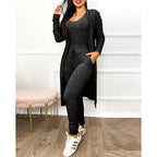 Femme en ensemble noir décontracté, cardigan long et pantalon ajusté, posant dans un intérieur moderne. Mode féminine, tenue confortable, style chic.