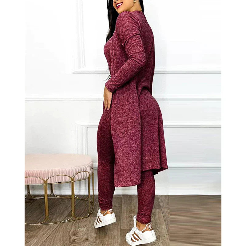 Femme portant un ensemble bordeaux élégant, composé d'une tunique longue et d'un legging, posant dans un intérieur moderne avec tabouret rose.