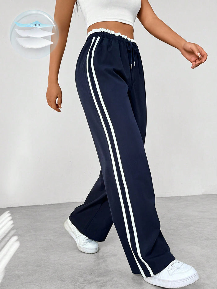 Femme portant un pantalon de jogging bleu marine à rayures blanches, taille élastique, avec baskets blanches. Mode décontractée, tendance sport.