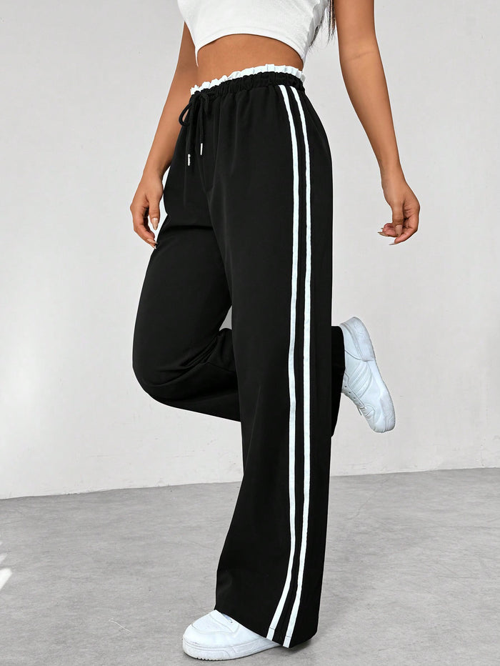 Pantalon de jogging noir à rayures blanches, femme, style décontracté, taille élastique, baskets blanches, mode sportive tendance.