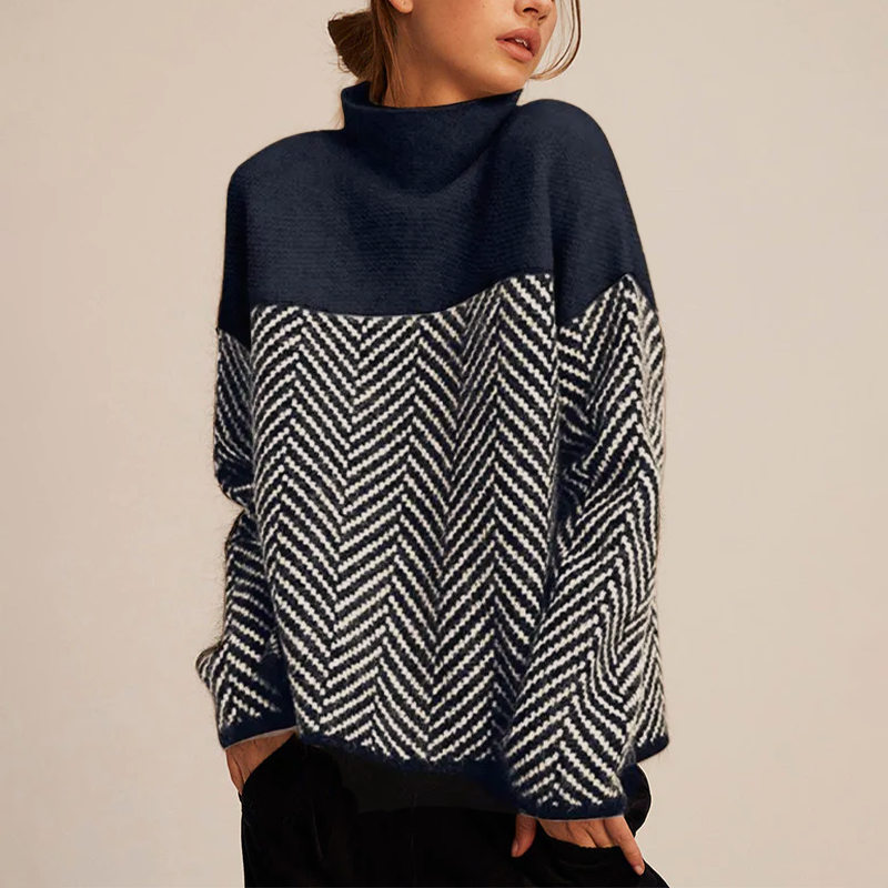 Femme portant un pull à col montant bleu marine avec motif chevron blanc et noir, mode automne-hiver, style décontracté et élégant.