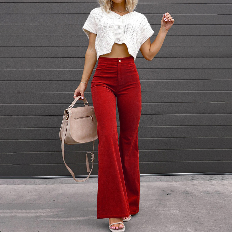 Femme en pantalon rouge évasé taille haute, top blanc court, tenant un sac beige. Mode élégante, tenue automne, style moderne.