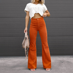 Femme portant un pantalon orange évasé taille haute et un haut blanc court, tenant un sac beige devant un mur gris. Mode automne chic.