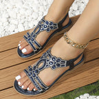 Sandales d'été ornées de perles bleues et strass, portées avec un bracelet chaîne doré sur une terrasse en bois, style chic et tendance.