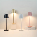 Quatre lampes de table modernes en noir, or, blanc et rose, posées sur une surface blanche, éclairant des livres empilés. Design élégant et minimaliste.
