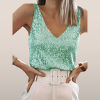 Femme portant un débardeur à paillettes vertes, ceinture blanche, pantalon blanc. Mode élégante, tenue chic, style moderne.