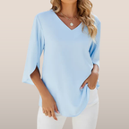 Blouse bleue à manches trois-quarts, col en V, portée par une femme. Mode féminine élégante, tenue décontractée, tendance printemps-été.