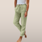 Pantalon en lin vert clair pour femme, taille élastique avec cordon, poches latérales, porté avec un débardeur blanc. Mode décontractée estivale.