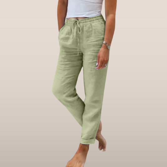 Pantalon en lin vert clair pour femme, taille élastique avec cordon, poches latérales, porté avec un débardeur blanc. Mode décontractée estivale.