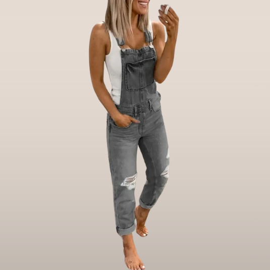 Femme souriante en salopette grise décontractée, tenant un smartphone. Mode tendance, look décontracté, style moderne.