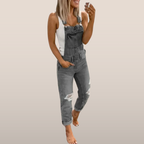 Femme souriante en salopette grise décontractée, tenant un smartphone. Mode tendance, look décontracté, style moderne.