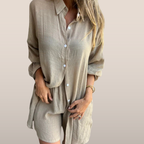 Femme portant une chemise ample beige en lin, manches longues, avec boutons blancs, style décontracté et élégant, mode estivale tendance.