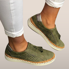 Chaussures décontractées vertes pour femmes, en cuir perforé, avec semelle en caoutchouc et détails en corde, portées avec un pantalon blanc.