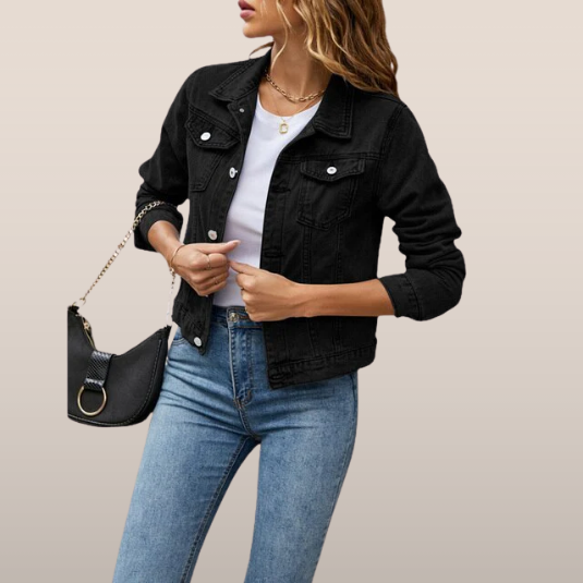 Femme portant une veste en jean noire, t-shirt blanc et jean bleu, tenant un sac à main noir. Mode décontractée, style tendance, look automne.