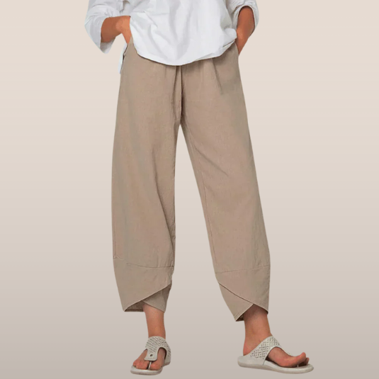 Pantalon ample beige en lin pour femme, coupe décontractée, avec ourlets asymétriques, porté avec des sandales tressées et une chemise blanche.