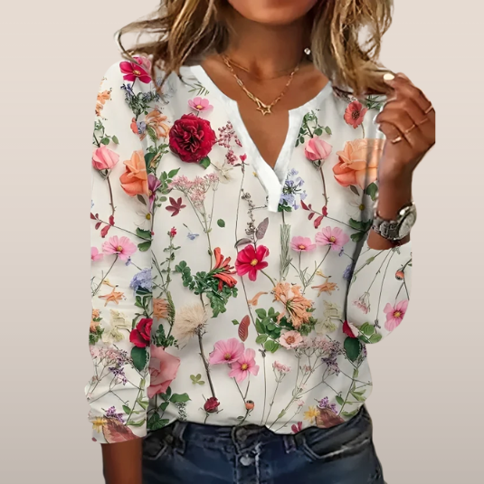 Blouse femme à manches longues avec motif floral coloré, fond blanc. Style décontracté, idéal pour mode printemps-été. Accessoires dorés visibles.
