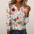 Blouse femme à manches longues avec motif floral coloré, fond blanc. Style décontracté, idéal pour mode printemps-été. Accessoires dorés visibles.