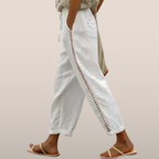 Pantalon blanc en lin avec broderie latérale, porté par une personne marchant en sandales. Mode estivale, style décontracté et élégant.