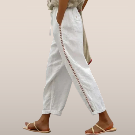 Pantalon blanc en lin avec broderie latérale, porté par une personne marchant en sandales. Mode estivale, style décontracté et élégant.