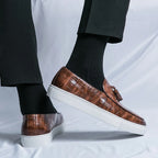 Chaussures mocassins en cuir marron à motif croco, semelle blanche, portées avec des chaussettes noires et un pantalon noir. Mode élégante masculine.