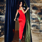 Femme en robe rouge élégante, entrant dans une pièce luxueuse avec rideaux sombres, talons hauts scintillants, ambiance glamour et sophistiquée.