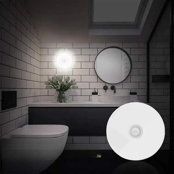 Salle de bain moderne avec lavabo blanc, miroir rond, carrelage mural noir et blanc, et bouquet de fleurs. Éclairage LED lumineux.