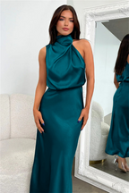 Robe longue en satin bleu-vert, sans manches, avec col drapé, portée par une femme devant un miroir. Mode élégante, tenue de soirée chic.