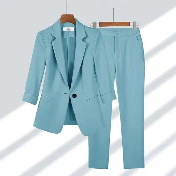 Costume femme bleu clair élégant, veste à manches longues et pantalon assorti, suspendu sur cintres en bois, mode professionnelle moderne.
