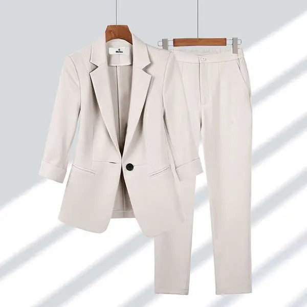 Costume femme beige élégant, veste à un bouton et pantalon assorti, suspendus sur cintres en bois, mode professionnelle chic.