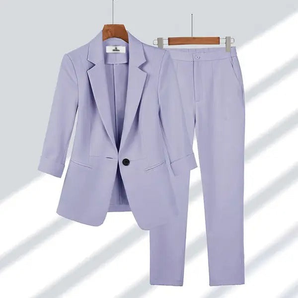 Costume femme lilas élégant, veste à un bouton et pantalon assorti, suspendus sur cintres. Mode professionnelle, tenue de bureau chic.