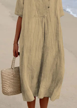 Robe en lin beige sur plage, tenue d'été élégante, sac en osier, mode féminine décontractée, style bord de mer, vêtements légers et confortables.