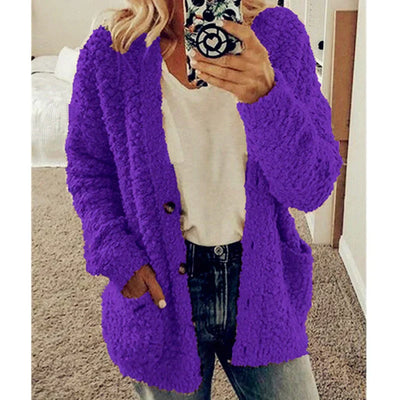 Femme portant un cardigan en laine violet, tenant un smartphone, vêtue d'un t-shirt blanc et d'un jean, dans une chambre moderne.