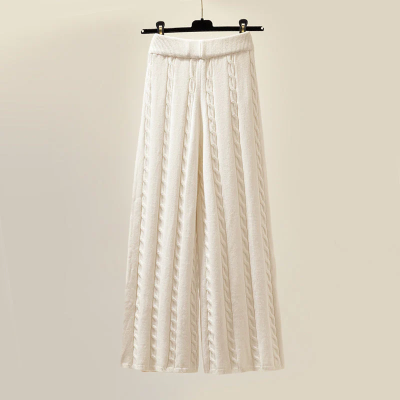 Pantalon large en tricot blanc, motif torsadé, suspendu sur un cintre noir. Mode féminine, style décontracté, tendance automne-hiver.