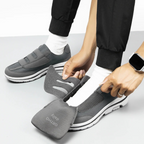 Personne ajustant des chaussures orthopédiques grises avec semelles amovibles, portant des chaussettes blanches et un pantalon noir. Montre connectée visible.