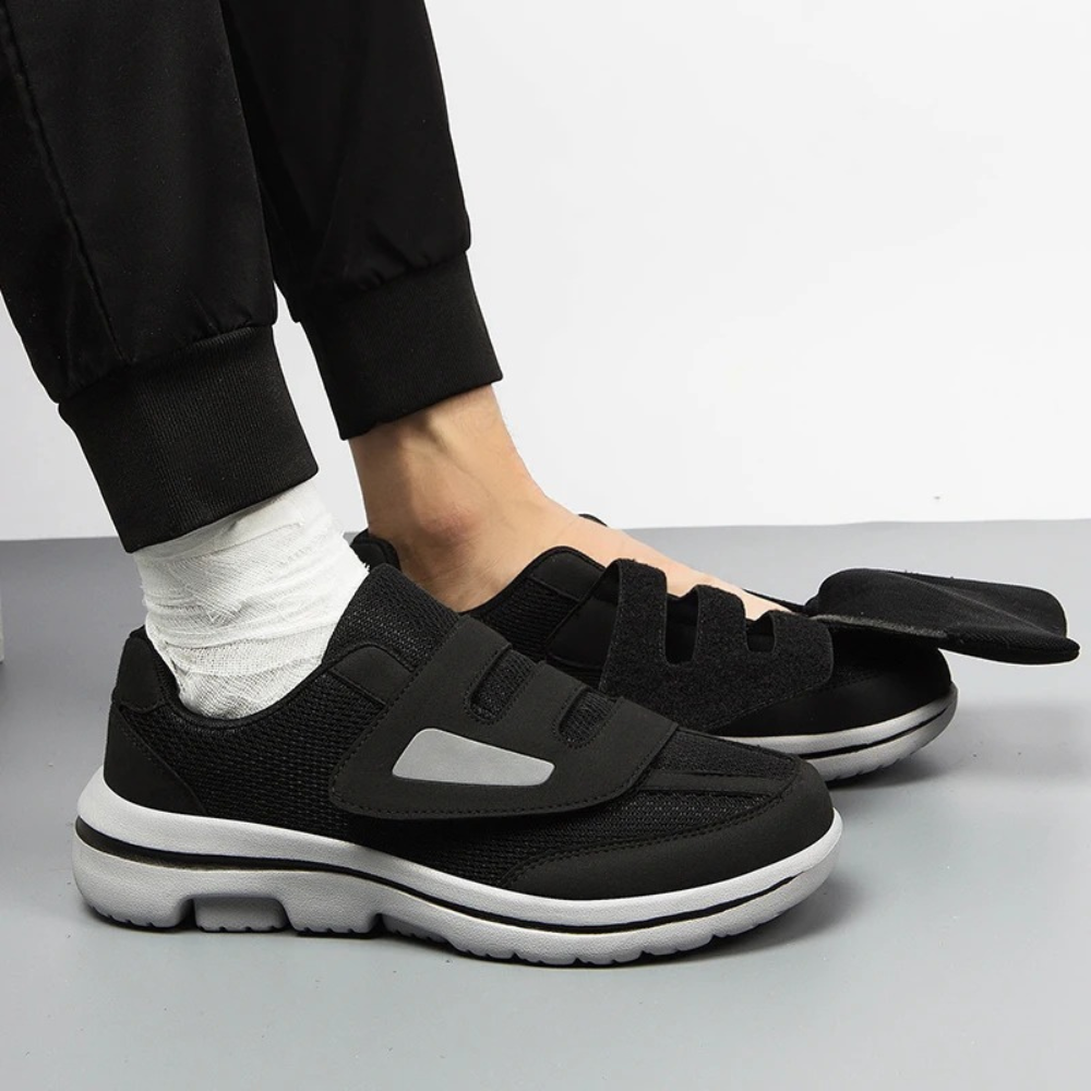 Chaussures orthopédiques noires pour homme avec fermeture velcro, semelle blanche antidérapante, portées avec un bandage au pied gauche.