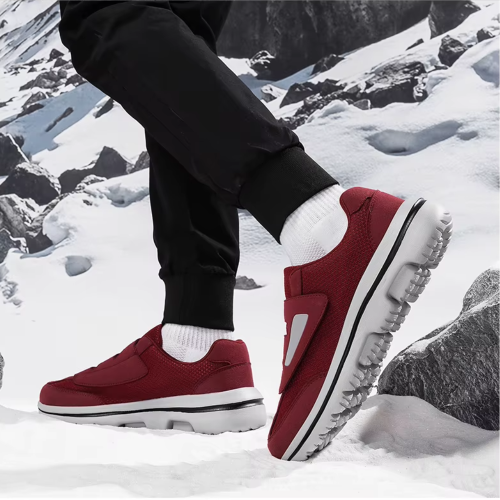 Chaussures de sport rouges sur neige, semelles antidérapantes, homme en pantalon noir, paysage montagneux enneigé, confort et style hivernal.