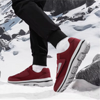 Chaussures de sport rouges sur neige, semelles antidérapantes, homme en pantalon noir, paysage montagneux enneigé, confort et style hivernal.